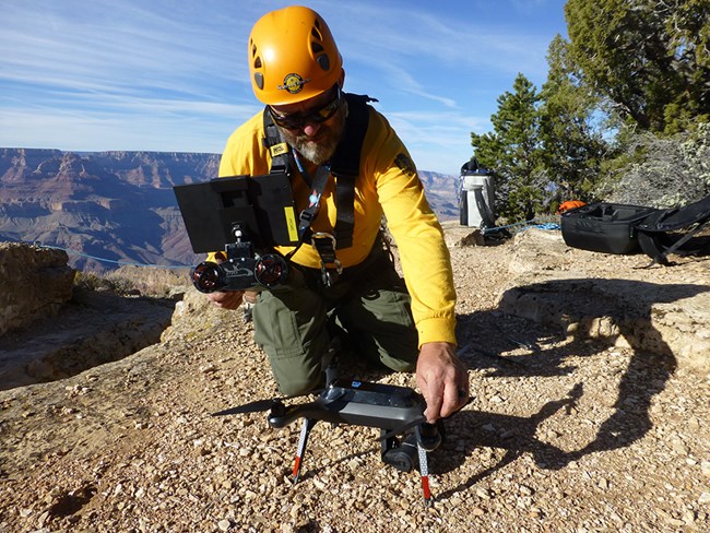 A man in Nomex and hardhat has a hand on quadcopter and controls.